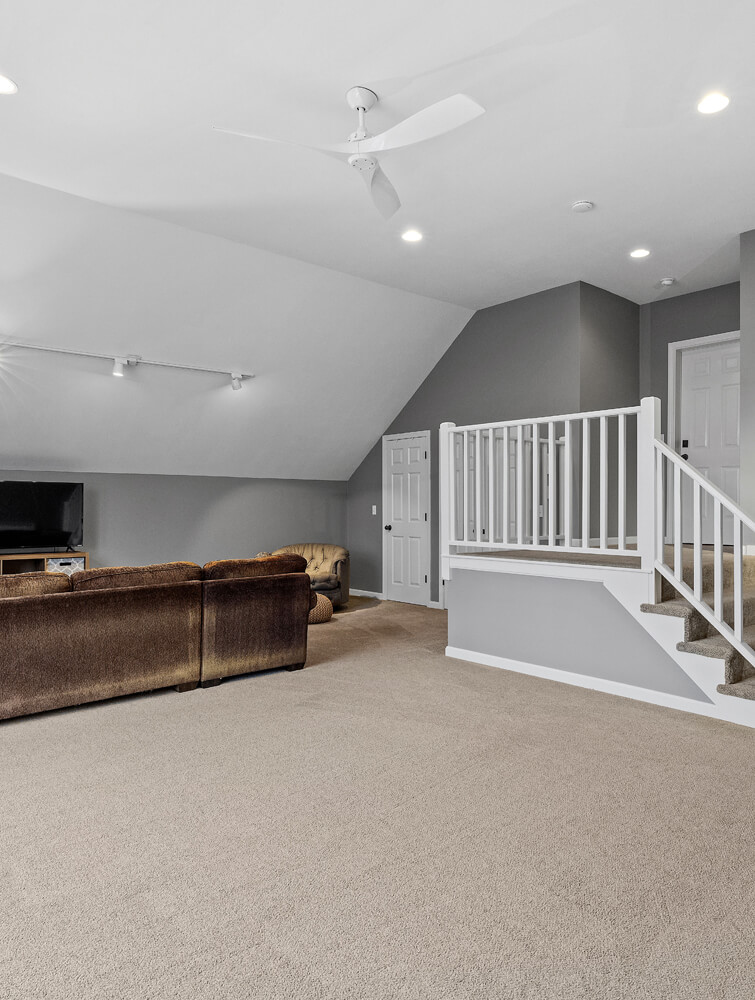 Finished basement or bonus room remodel by SC Projects LLC featuring beige carpet, gray walls, white trim, and a white staircase railing.