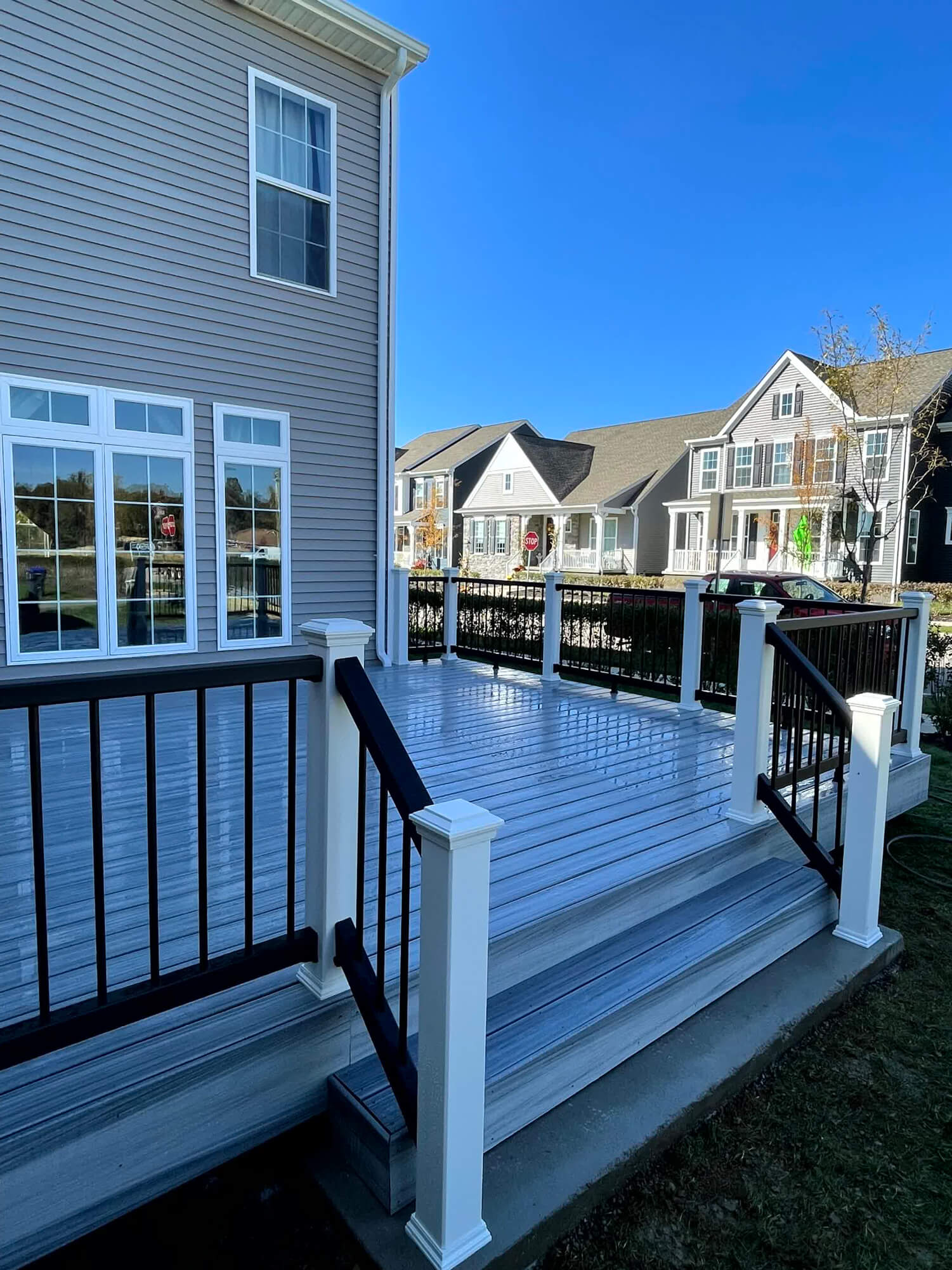 Newly constructed gray composite deck by SC Projects LLC with black metal railings and white posts attached to a gray vinyl-sided house.