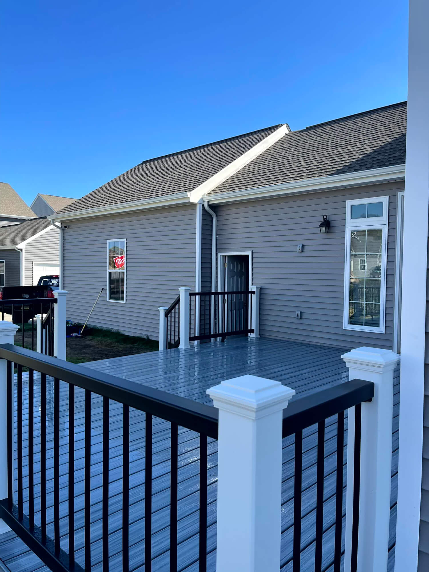Newly constructed gray composite deck by SC Projects LLC with black metal railings and white posts attached to a gray vinyl-sided house.