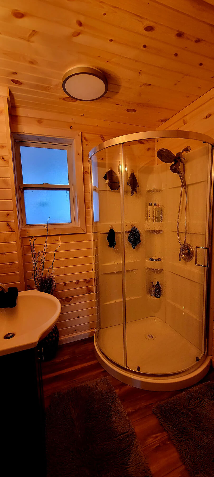 Modern bathroom remodel by SC Projects LLC featuring a walk-in shower with glass doors, gray vanity, white countertop, and light wood-look plank flooring.
