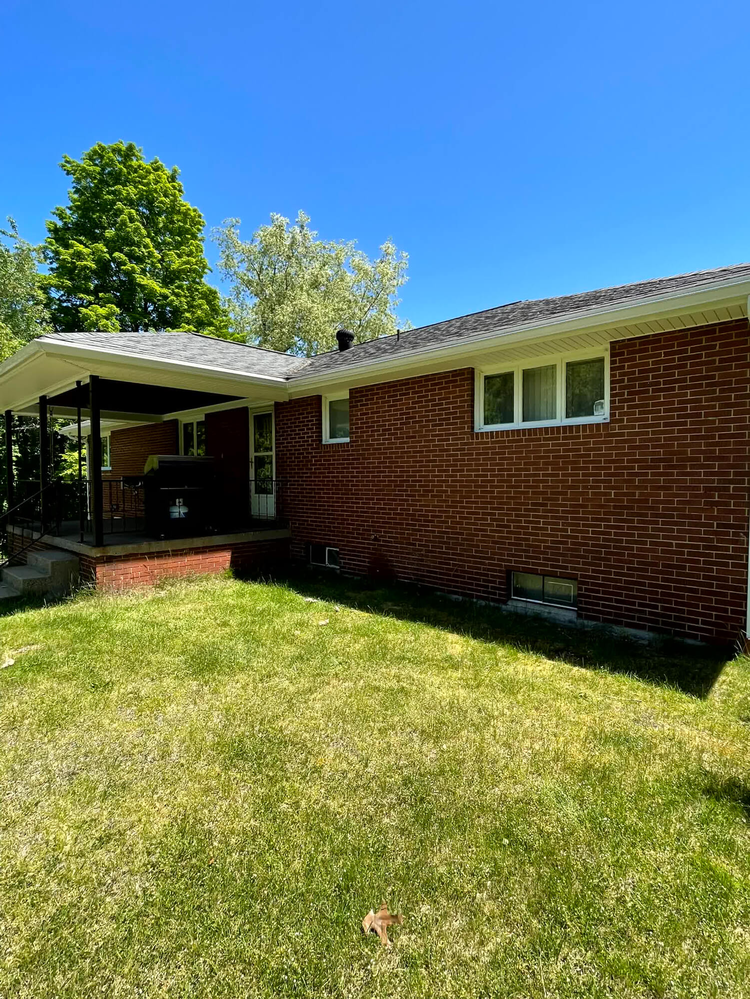 The red brick home features a newly installed gray shingle roof and white gutters,