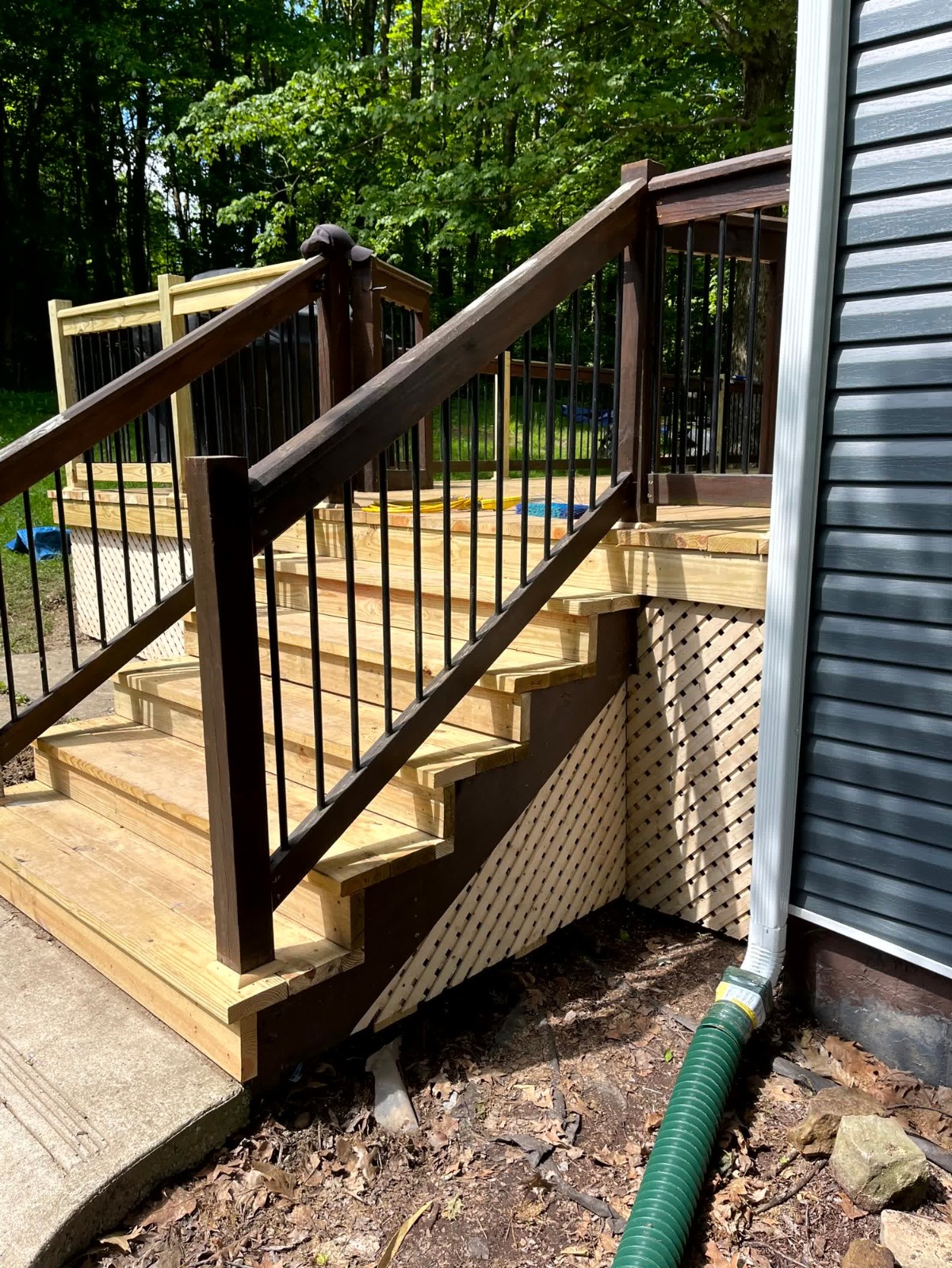 Finished composite deck by SC Projects LLC with light gray planks, white posts, and black metal balusters on a gray vinyl-sided house .
