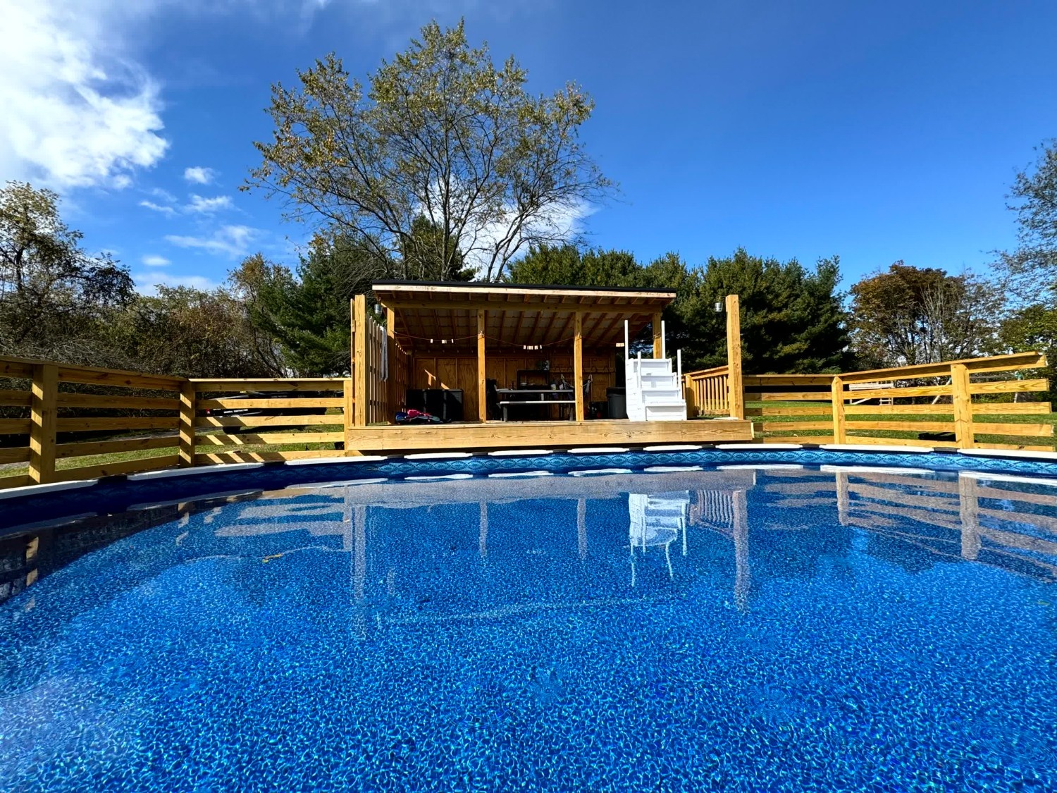 Outdoor wooden deck and covered cabana built by SC Projects LLC surrounding an above-ground swimming pool under a blue sky .