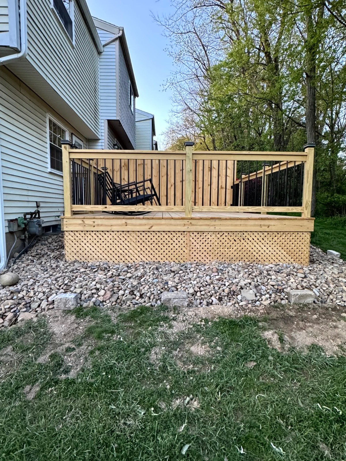 Elevated wooden deck structure by SC Projects LLC with brown composite railings supported by wooden posts next to a light gray vinyl house and brick foundation .