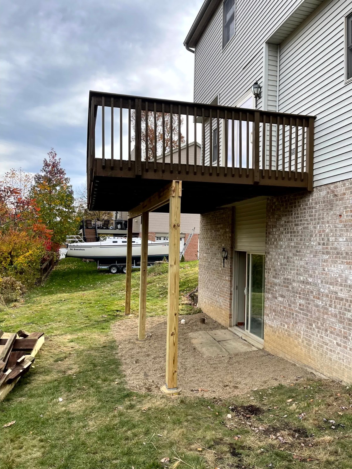Covered outdoor living space by SC Projects LLC featuring rich brown decking, white posts, and dark railings against a red brick house .
