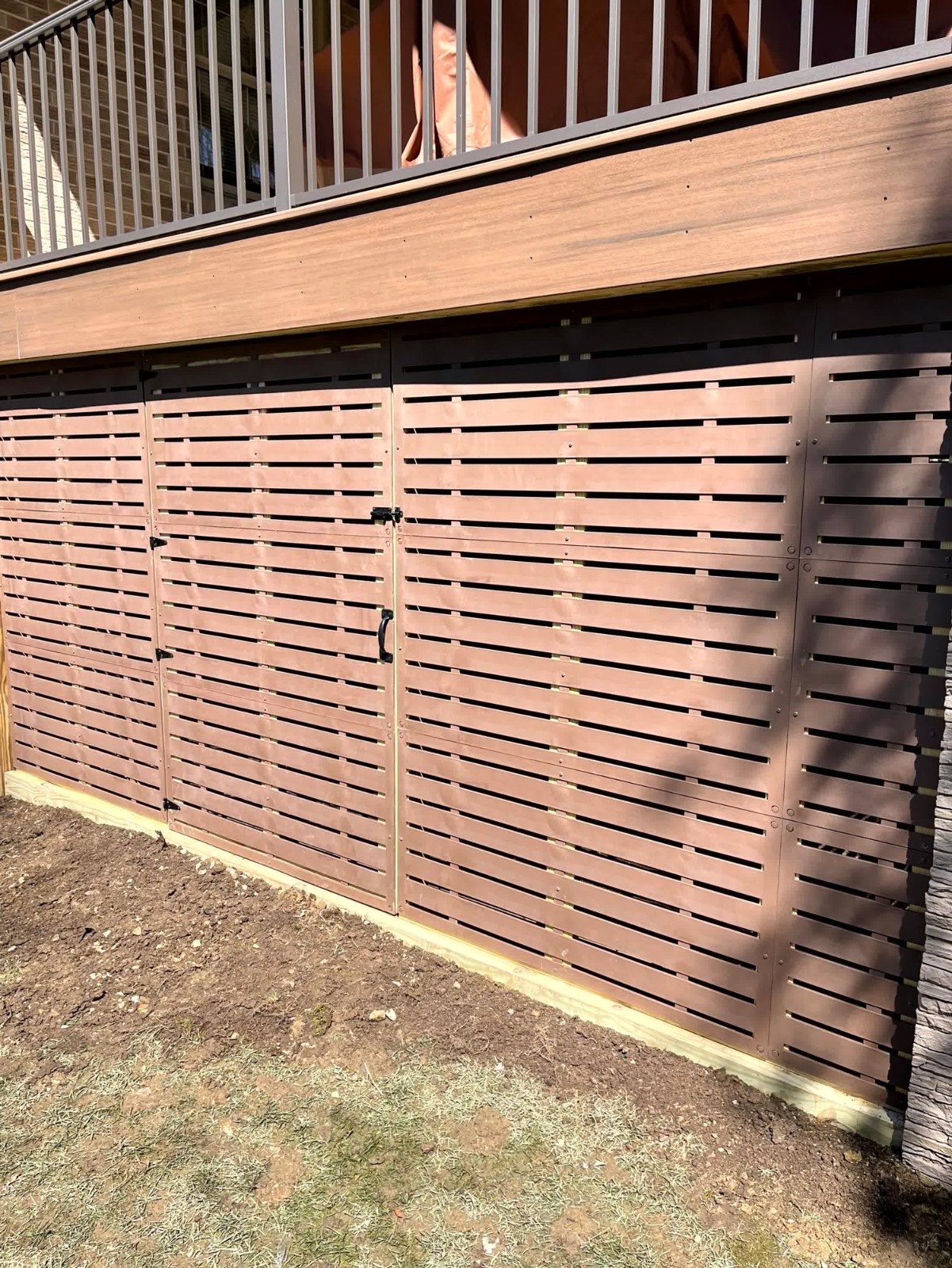 Composite deck skirting with horizontal brown slats and a hidden access door installed by SC Projects LLC .