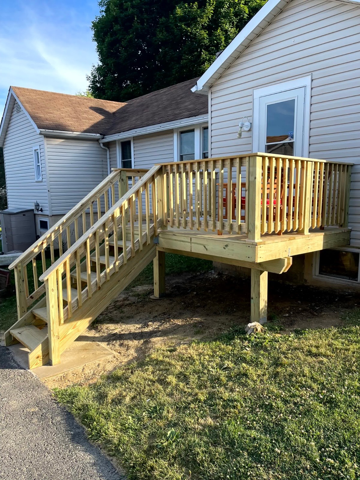 Finished low-profile wooden deck by SC Projects LLC with black metal balusters and wood railings against a red brick house .