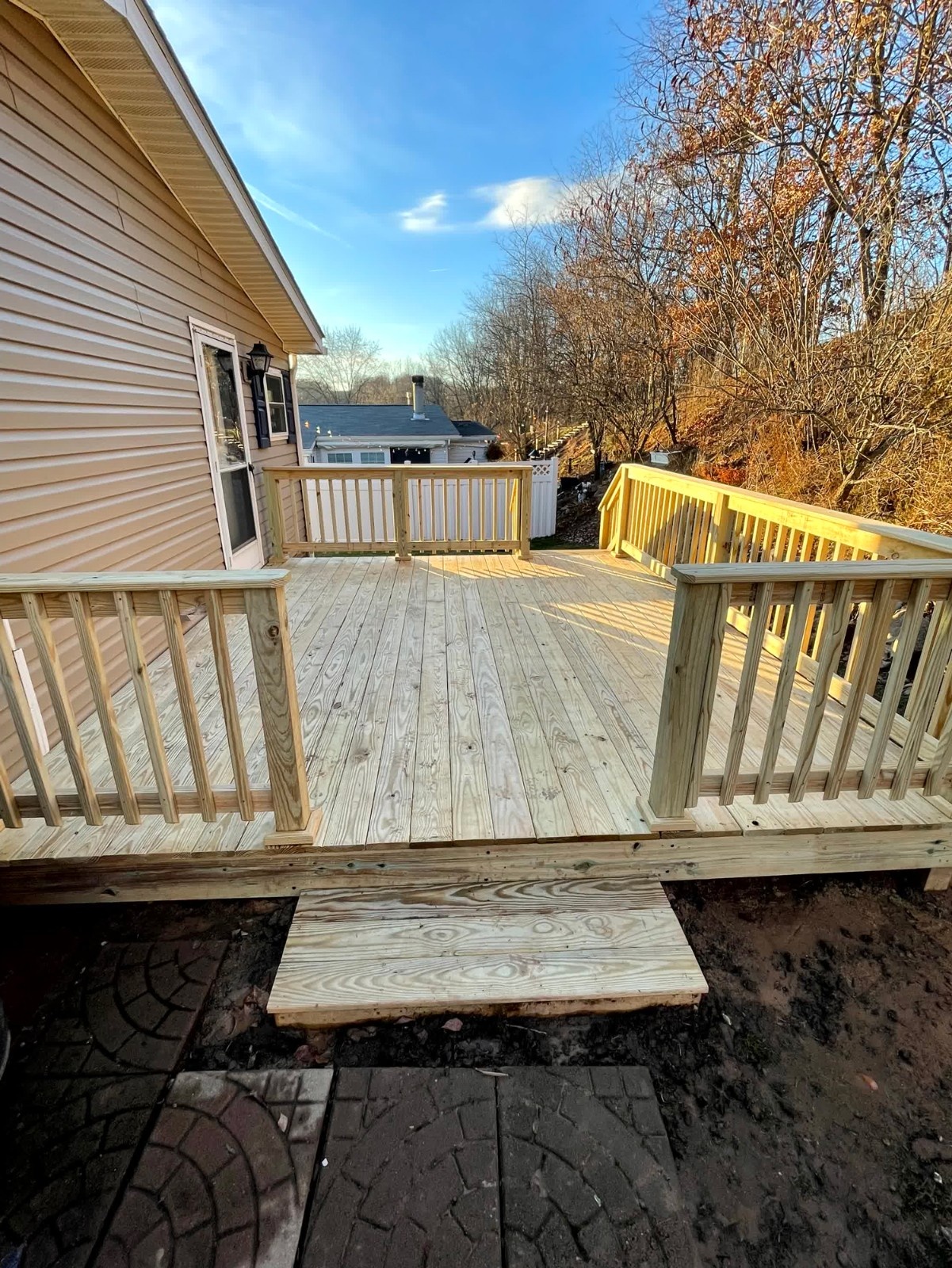 Finished covered porch and deck installation by SC Projects LLC featuring rich brown decking, white posts, and dark railing balusters on a red brick home .