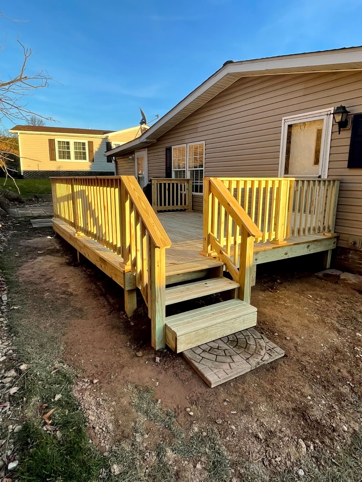 New wooden deck construction by SC Projects LLC with corner stairs and full wood railings attached to a tan vinyl sided home .
