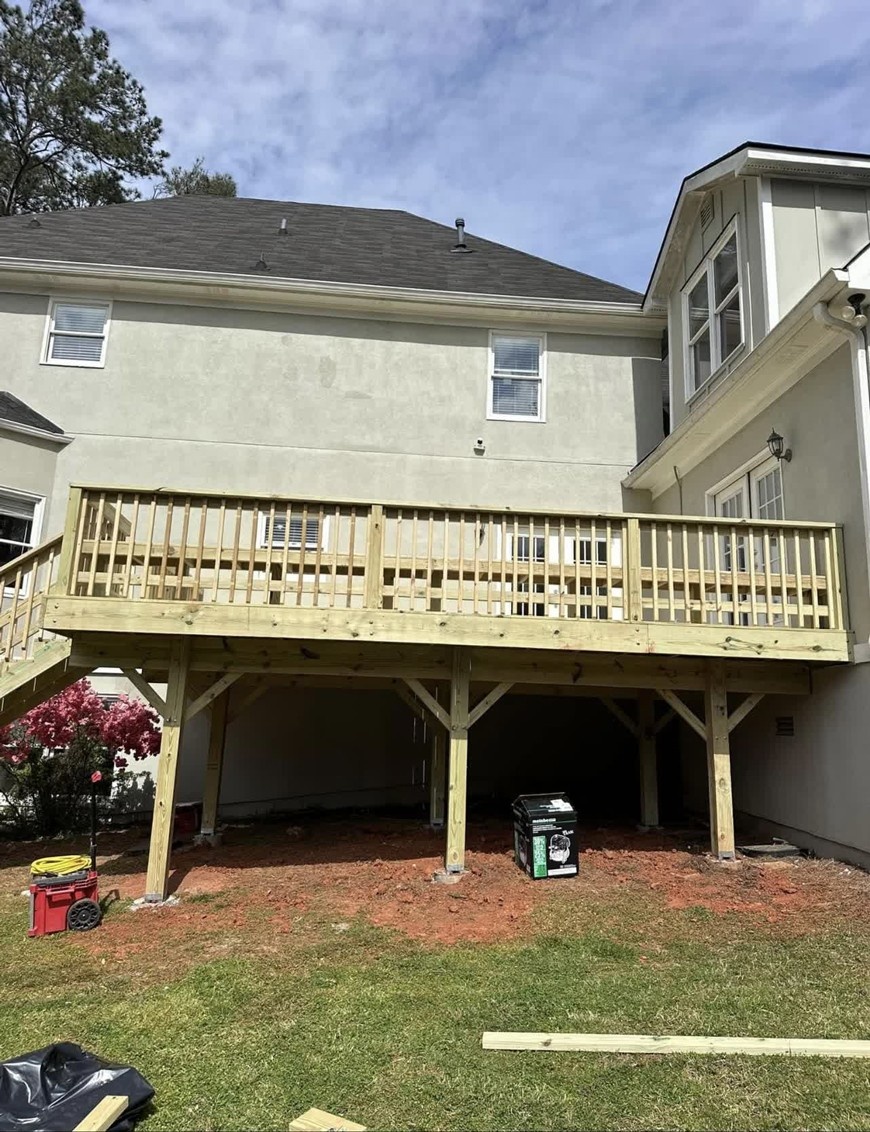 New wooden deck construction by SC Projects LLC extending from a stucco house with dark shingle roofing and wooden railings .