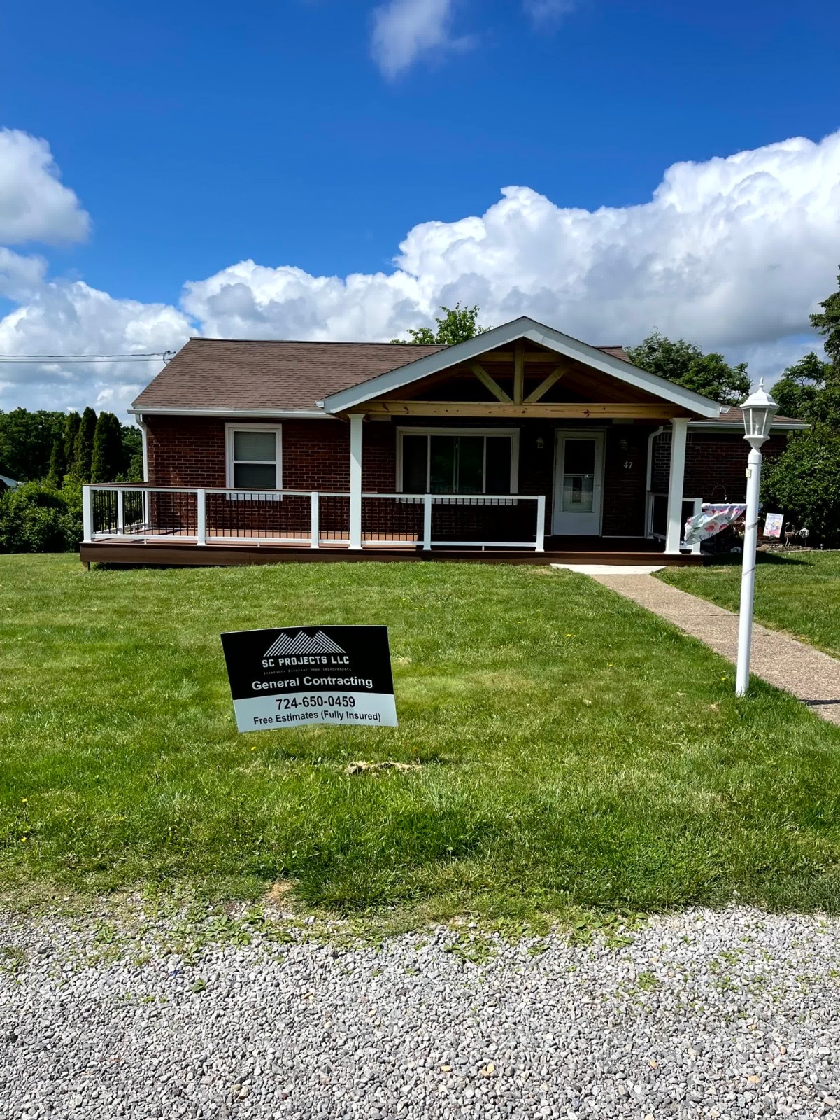 Completed deck installation and covered porch by SC Projects LLC on a brick home with white railings and asphalt shingle roof .
