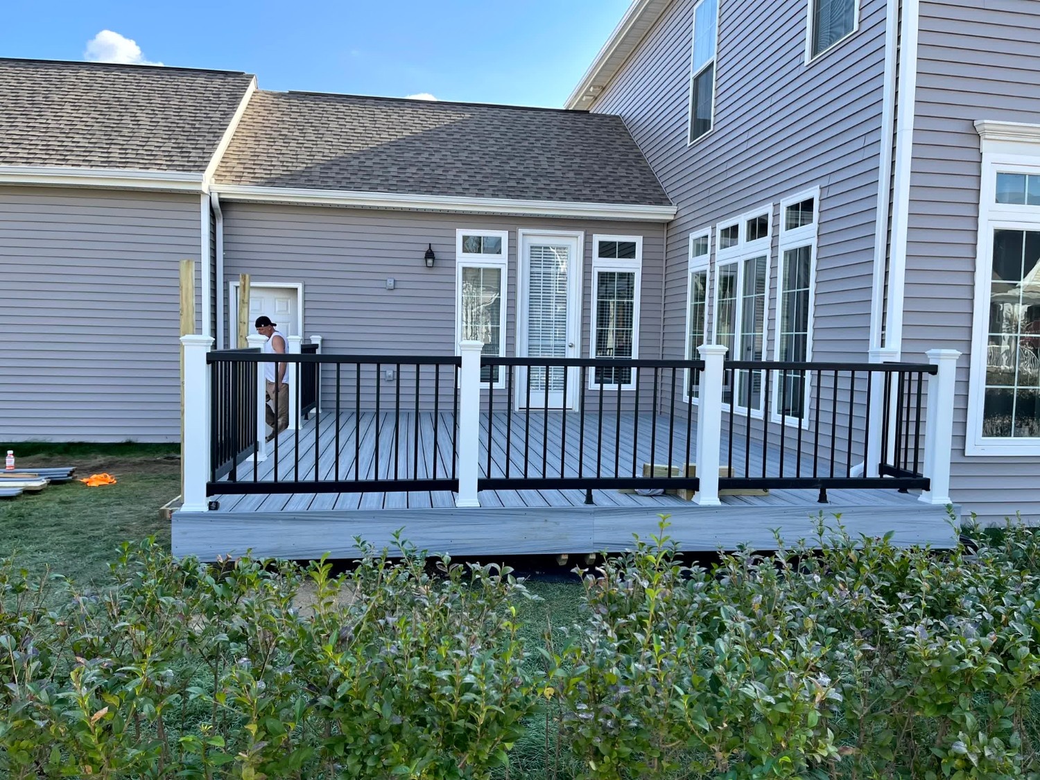 Finished elevated wooden deck by SC Projects LLC with matching railing and post supports on a gray vinyl-sided home with a walk-out basement .