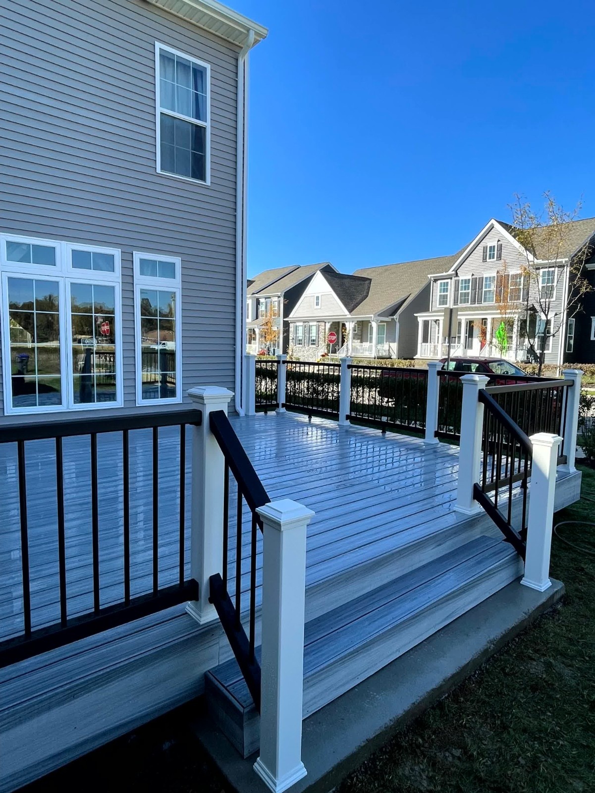 Finished covered porch and deck installation by SC Projects LLC with brown composite decking, white posts, and dark railing balusters on a red brick home .