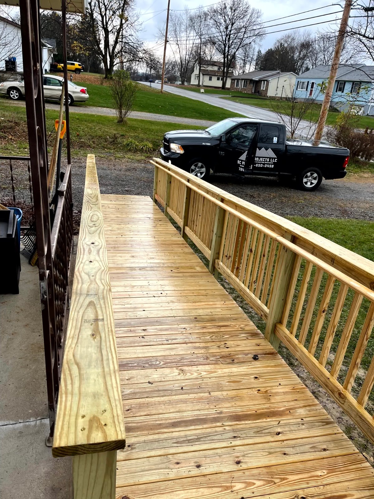 Composite deck landing and stairs by SC Projects LLC featuring dark brown planks, white posts, and black metal balusters facing a grassy backyard .