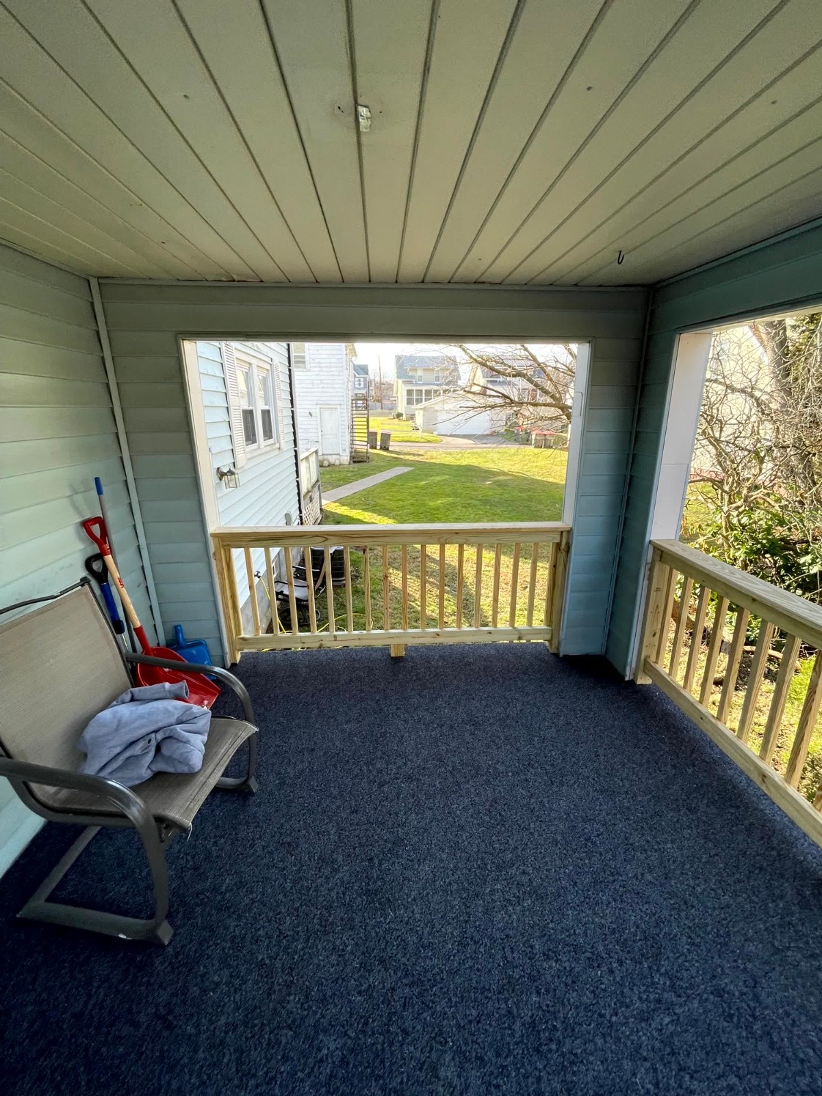 Stairs leading down from a composite deck by SC Projects LLC with white posts and black balusters against a green wooded backyard .