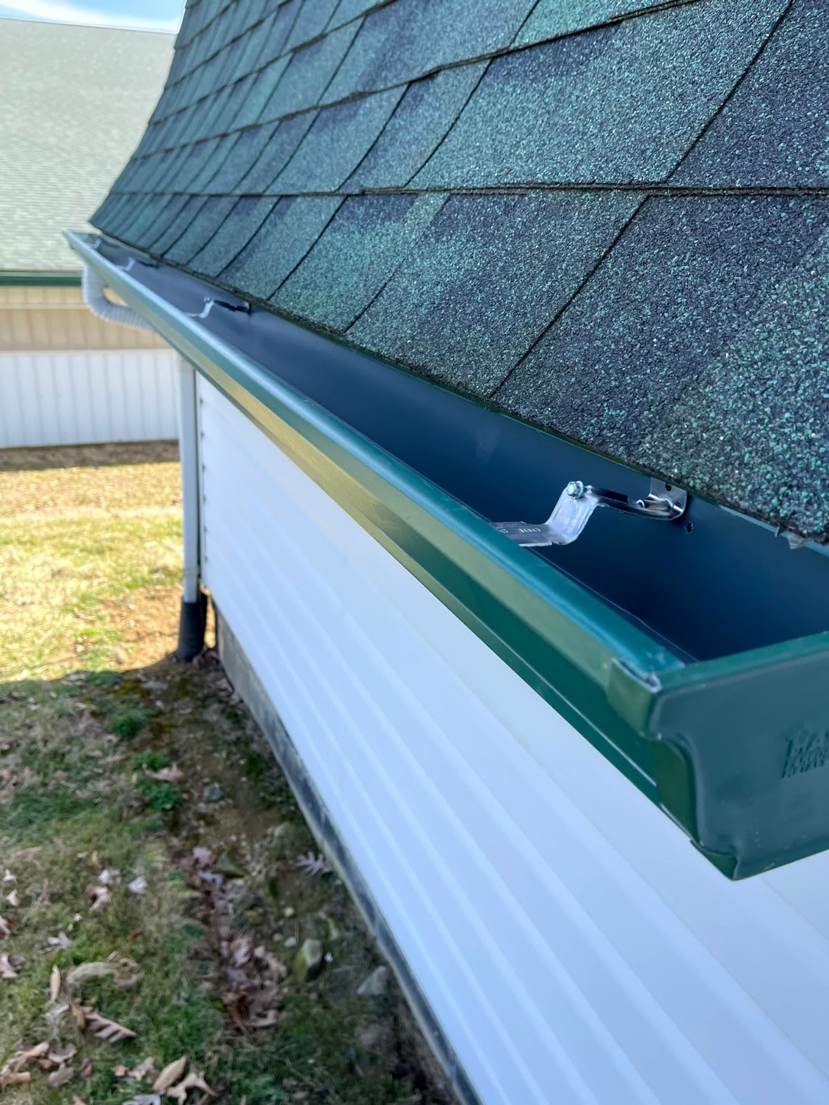 Green seamless gutter installation on a white barn with dark green shingles and hidden brackets .