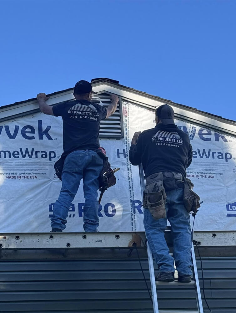 Crew members of SC Projects LLC on a ladder installing exterior siding and vent components on a home wrapped in Tyvek HomeWrap.