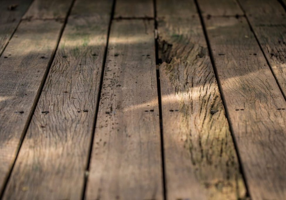 Low-profile wooden deck by SC Projects LLC with brown composite railings and lattice skirting surrounded by decorative river rock .